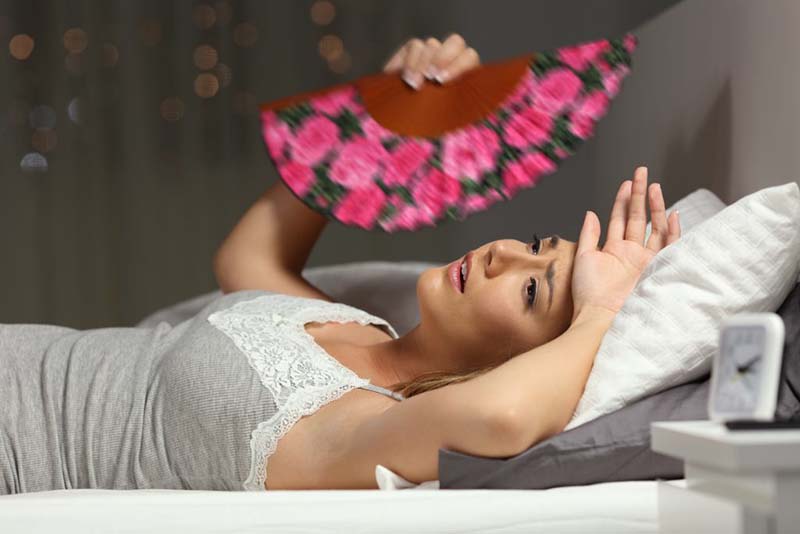 Tips for getting to sleep - Woman lying in bed with fan to keep cool